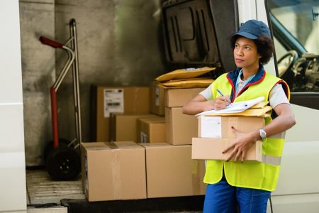 Courrier afro-américain féminin se préparant pour la livraison et vérifiant la liste des colis par fourgon de livraison
