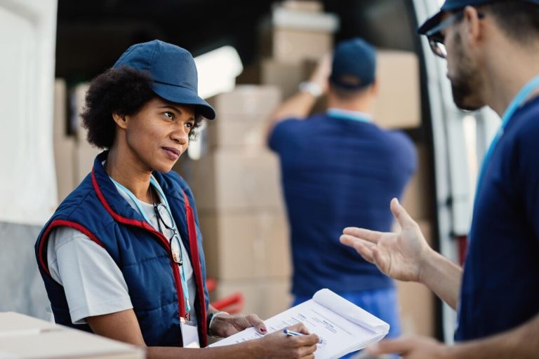 Deux livreurs communiquent et passent par la paperasse pendant que leurs collègues chargent des colis dans une camionnette L'accent est mis sur une femme afro-américaine