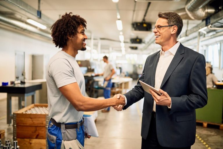 Heureux ingenieur et jeune travailleur noir se serrant la main tout en saluant dans un batiment industriel